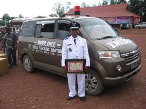 Kepala Desa Tanjung Bantur dengan piagam penghargaan di depan ambulans desa